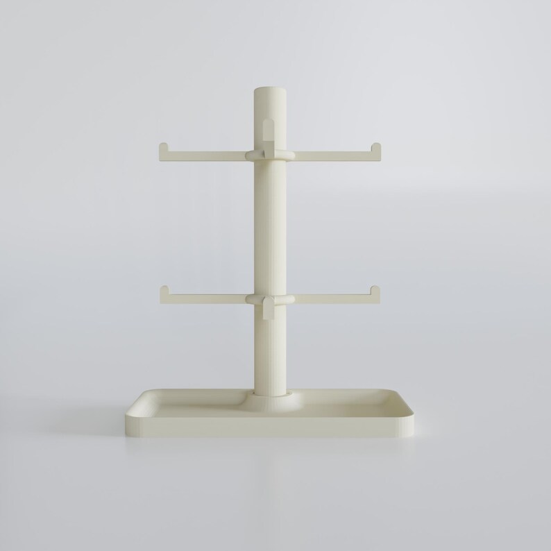 May include: A cream-colored mug tree with a rectangular base, a central pole, and two tiers of hooks for hanging mugs. The top of the pole has a small handle. The design is minimalist and modern.