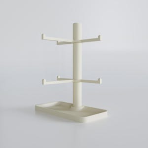 May include: A cream-colored mug tree with a rectangular base and a central pole. The pole has two tiers of horizontal arms for hanging mugs. The top of the pole has a smaller, cylindrical extension.