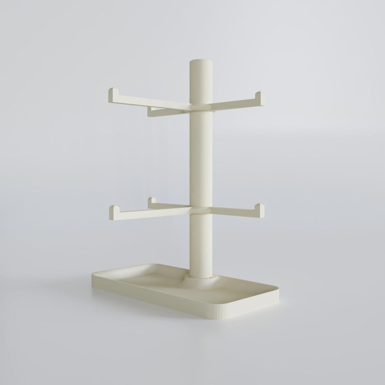 May include: A cream-colored mug tree with a rectangular base and a central pole. The pole has two tiers of horizontal arms for hanging mugs. The top of the pole has a smaller, cylindrical extension.