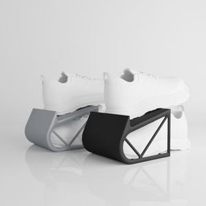 Peut inclure: Trois paires de baskets blanches sont présentées sur des présentoirs à chaussures modernes. Les présentoirs sont gris et noirs, avec un design incurvé et une structure de support géométrique. Les baskets ont une esthétique minimaliste.