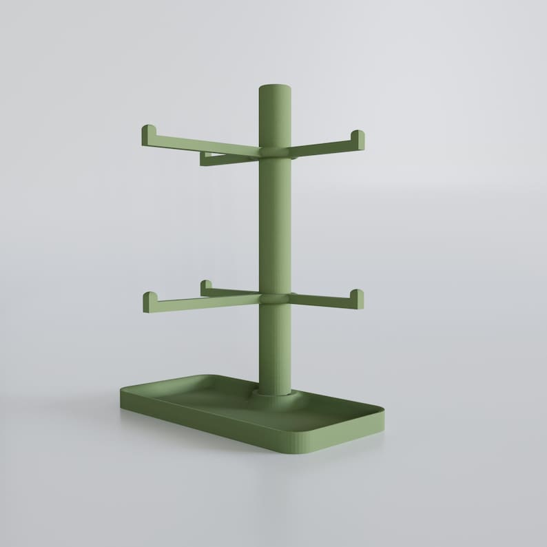 May include: A sage green mug tree with a rectangular base and two tiers of horizontal arms for hanging mugs. The central pole extends upwards, with a top section for additional storage. The design is minimalist and modern.