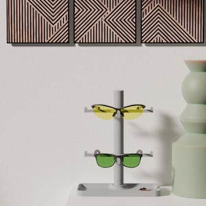 May include: Three geometric wooden wall art panels with black frames and a light wood grain pattern. A gray sunglasses display stand holds yellow and green lens sunglasses. A green vase is on the right.