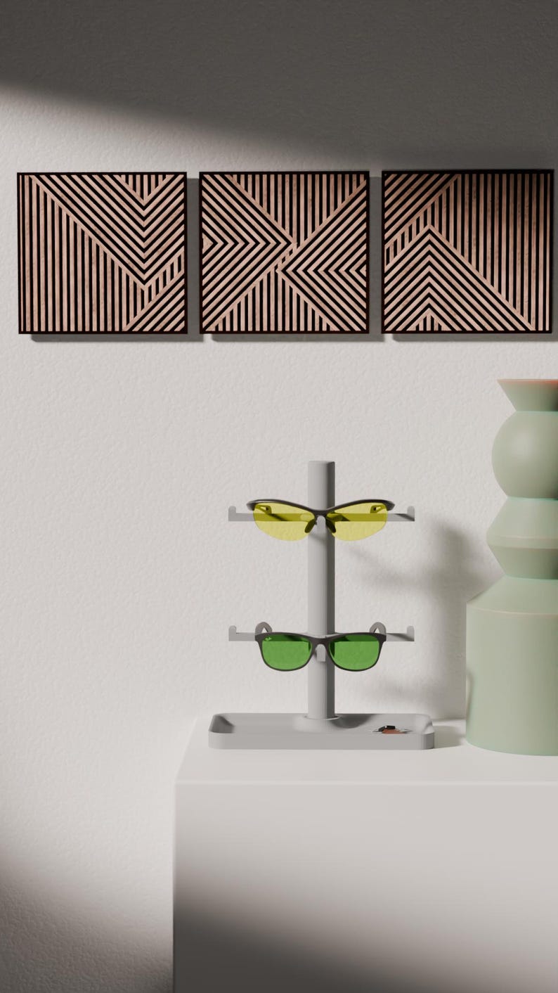 May include: Three geometric wooden wall art panels with black frames and a light wood grain pattern. A gray sunglasses display stand holds yellow and green lens sunglasses. A green vase is on the right.