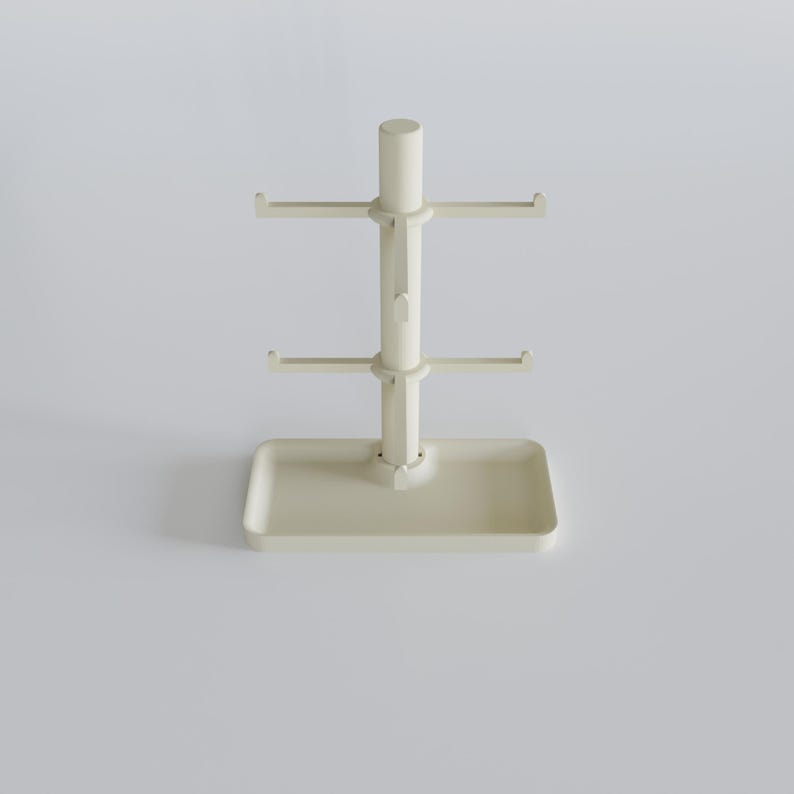 May include: A cream-colored mug tree with a rectangular base and a central pole. The pole has two tiers of hooks for hanging mugs, and a cylindrical top. The design is minimalist and functional, suitable for kitchen organization.