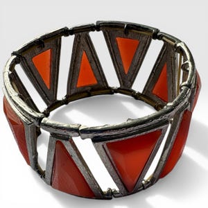 May include: A silver-coloured bracelet with orange triangular shapes. The triangles are set within a silver metal frame, creating an open, geometric design. The bracelet appears to be made of metal and plastic.