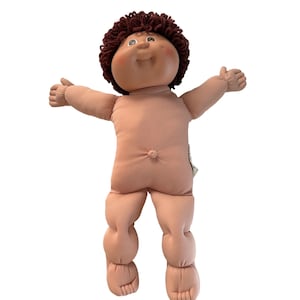 Könnte beinhalten: Eine weiche Puppe mit einem runden, pfirsichfarbenen Gesicht, Grübchen an den Wangen und einer kleinen Nase. Die Puppe hat kurzes, lockiges, dunkelbraunes Wollhaar, blaue Augen und ein Lächeln. Sie besitzt einen Stoffkörper mit Bauchnabel und Armen.