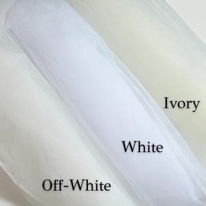 May include: Close-up of three rolls of tulle fabric in Off-White, White, and Ivory. The names of the colors are printed on the fabric. The tulle is a sheer, lightweight material often used for bridal wear and crafts.