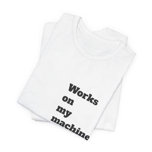 Puede incluir: Dos camisetas blancas dobladas, con la superior mostrando el texto "Works on my machine" en negro y negrita. Las camisetas parecen estar hechas de un tejido suave, probablemente algodón.