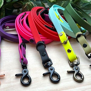 Könnte beinhalten: Eine Auswahl an bunten Hundeleinen in Lila, Pink, Rot, Blau und Grün. Jede Leine hat einen passenden Karabiner und Beschläge. Die Leinen bestehen aus einem strapazierfähigen, flexiblen Material.