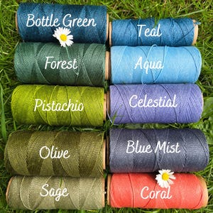 May include: Ten spools of thread arranged in two columns, labeled Bottle Green, Teal, Forest, Aqua, Pistachio, Celestial, Olive, Blue Mist, Sage, and Coral. Each spool features a textured, wound cord and a small white daisy flower accent.