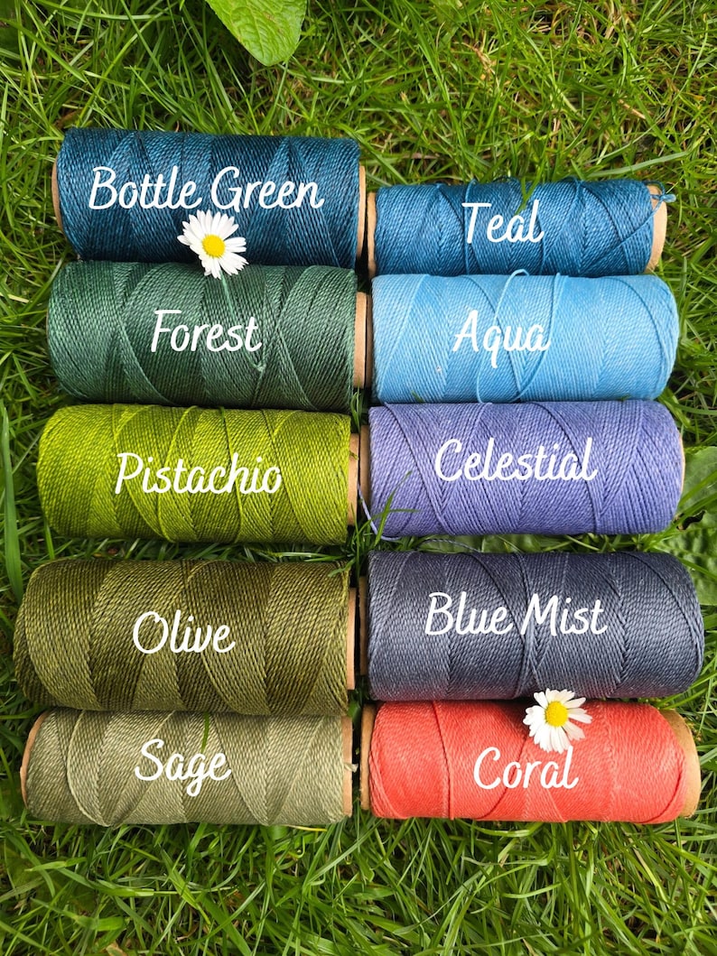 May include: Ten spools of thread arranged in two columns, labeled Bottle Green, Teal, Forest, Aqua, Pistachio, Celestial, Olive, Blue Mist, Sage, and Coral. Each spool features a textured, wound cord and a small white daisy flower accent.