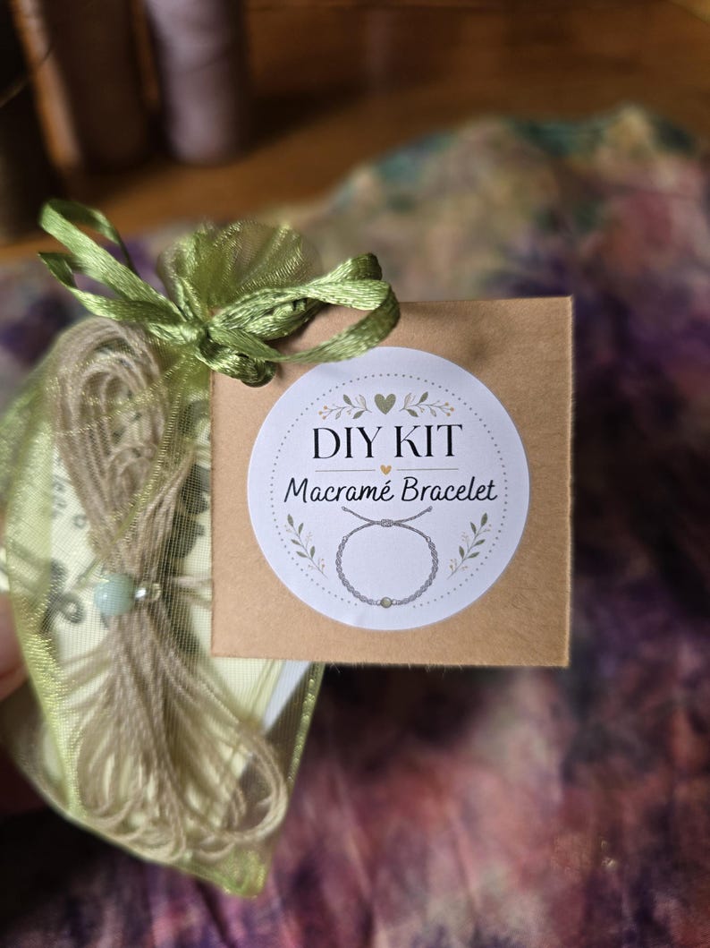 May include: A DIY kit for a macram&eacute; bracelet packaged in a sheer light green organza drawstring bag. A square brown cardboard tag is attached to the bag, featuring a white circular sticker with the text DIY KIT Macram&eacute; Bracelet and a graphic.
