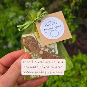 May include: A DIY macram&eacute; bracelet kit inside a sheer olive green organza drawstring pouch. A square brown tag features the text DIY KIT Macram&eacute; Bracelet and a line drawing of a bracelet. Brown cord and a single round bead are visible inside.