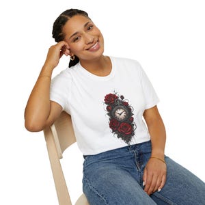 May include: A white short-sleeve t-shirt featuring a central graphic print of a vintage pocket watch surrounded by deep red roses and dark thorny vines. The design is detailed with intricate shading and realistic floral textures on the fabric.