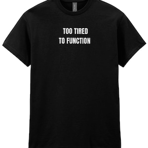 Puede incluir: Camiseta negra de cuello redondo con el texto blanco "TOO TIRED TO FUNCTION" impreso en el pecho. La camiseta está hecha de un material suave y tiene mangas cortas.