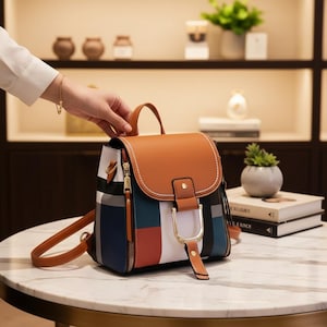 May include: A brown and multi-coloured backpack with a top handle and adjustable straps. The bag features a flap closure with a gold-coloured buckle and a zip pocket. The design includes a patchwork of colours, including white, blue, red, and brown.