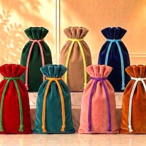 May include: A collection of seven velvet drawstring pouches in various colors including red, dark green, tan, navy blue, teal, pink, and orange. Each pouch features a contrasting colored cord closure tied in a bow at the top of the bag.