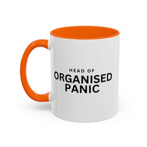 May include: A white ceramic mug with a bright orange interior and handle. The front of the mug features the black text "HEAD OF ORGANISED PANIC" printed in a bold, sans-serif font. The mug has a cylindrical shape with a smooth, glossy finish.