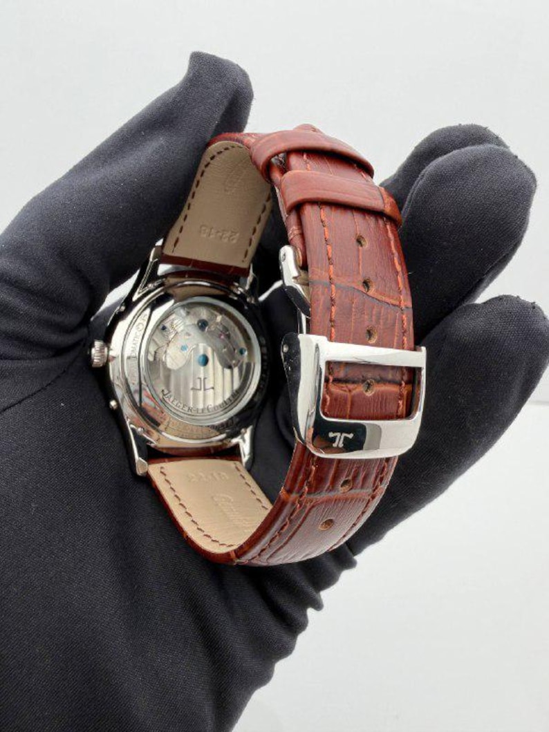 May include: A luxury wristwatch with a brown leather strap and a silver buckle. The watch face is visible, showcasing the intricate internal mechanisms. The watch has a silver case and a brown leather strap.