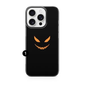 K&ouml;nnte beinhalten: Schwarze Handyh&uuml;lle mit einem Halloween-Design. Die H&uuml;lle hat einen schwarzen Hintergrund mit einem orangefarbenen, stilisierten Grinsegesicht. Die Handyh&uuml;lle hat einen transparenten Rand und einen Kameraausschnitt.