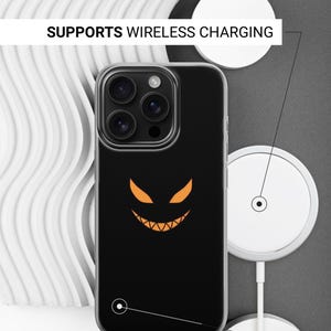 K&ouml;nnte beinhalten: Schwarze Handyh&uuml;lle mit transparentem Rand, mit einem orangefarbenen K&uuml;rbisgesicht-Design. Die H&uuml;lle unterst&uuml;tzt kabelloses Laden. Der Text auf dem Bild lautet: "SUPPORTS WIRELESS CHARGING" und "SIDES ARE NOT PRINTED".