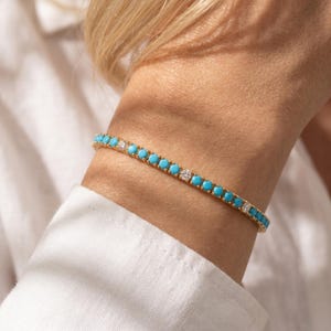 May include: A gold-toned tennis bracelet featuring a repeating pattern of round, bright turquoise stones interspersed with clear, sparkling white stones. The bracelet is designed with a delicate metal chain setting that holds each stone securely.