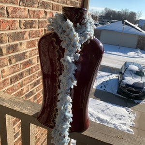 Puede incluir: Una bufanda esponjosa de color azul claro con un patrón marrón y blanco, expuesta en un maniquí rojo. La bufanda está colgada en una barandilla de madera.
