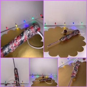 May include: A close-up of a red, black, and silver crochet hook with a white cord attached. The hook is lying on a gold surface.
