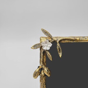 Peut inclure: Un coin de cadre dor&eacute; avec un motif floral et de feuilles. Le cadre pr&eacute;sente une fleur argent&eacute;e et des accents de feuilles d&eacute;taill&eacute;s. L'int&eacute;rieur du cadre est gris fonc&eacute;.