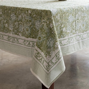 Op de afbeelding: Een rechthoekig tafelkleed met een ingewikkelde botanische print in saliegroen en wit. De stof toont een dicht patroon van gestileerde bloemen en bladeren, afgewerkt met een brede rand met een gestreept detail aan de zijkant.