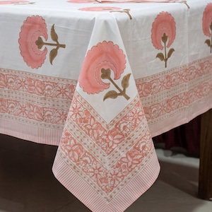 May include: A white tablecloth featuring a repeating pattern of large, soft pink flowers with brown stems and leaves. The border displays a detailed floral print in shades of pink and brown, finished with a thin, striped edge in light pink and white.