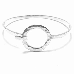 Peut inclure: Un bracelet jonc argenté avec une texture martelée. Le bracelet présente un motif circulaire martelé au centre et une fermeture à crochet. Un bijou simple et élégant.