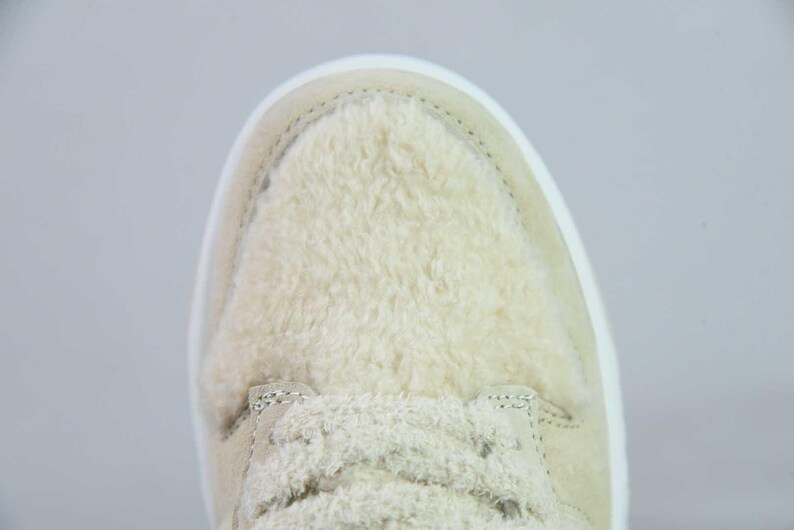 Peut inclure: Gros plan d'une basket beige avec une tige textur&eacute;e et duveteuse. La chaussure est dot&eacute;e d'une semelle et de lacets blancs. Le design est simple, mettant l'accent sur la mati&egrave;re douce et moelleuse.