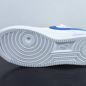 May include: White and blue athletic shoe, seen from the sole. The shoe has a white rubber sole with a circular tread pattern and the Nike logo. A blue accent stripe is visible on the upper.