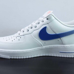 May include: White leather trainer with a blue swoosh and detailing. The shoe has a white sole and a perforated toe. A classic athletic shoe.