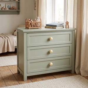 May include: A sage green wooden dresser featuring three horizontal drawers, each equipped with a single round, light-colored wooden knob. The piece has a clean, rectangular frame and sits on four short, sturdy legs, providing a stable storage solution.
