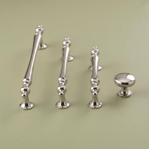 May include: A set of four polished silver-toned cabinet hardware pieces, including three elongated drawer pulls of varying lengths and one round cabinet knob. Each piece features a smooth, reflective metallic finish and a classic, rounded design.