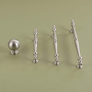 May include: A set of cabinet hardware in a brushed silver finish, consisting of one round spherical knob and three elongated drawer pulls of varying lengths, each featuring a central tapered bar with decorative rounded accents at the ends.