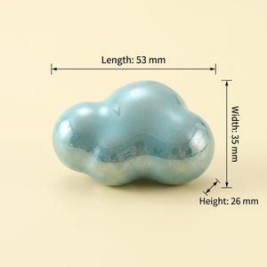 May include: A smooth, iridescent light blue cloud-shaped object with a glossy finish. Technical annotations indicate a length of 53 mm, a width of 35 mm, and a height of 26 mm. The object has a rounded, organic form with multiple bulbous sections.