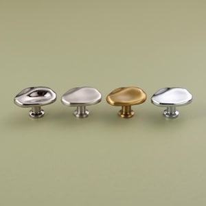 May include: Four cabinet knobs with irregular, organic, pebble-like shapes. The set includes one polished dark chrome, one matte silver, one brushed gold, and one polished bright silver finish, each featuring a central cylindrical base.