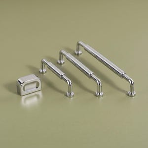 May include: A set of three polished chrome cabinet pulls of varying lengths and one matching rectangular knob. Each pull features a cylindrical bar supported by two vertical posts with circular bases, providing a sleek and reflective metallic finish.