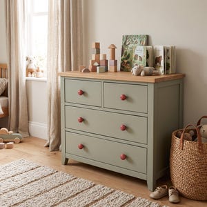 May include: A sage green wooden dresser with a natural wood top surface, featuring two small top drawers and two full-width bottom drawers. Each drawer is equipped with a round, reddish-brown knob. The dresser stands on four short legs.