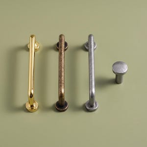 May include: Three metal cabinet pulls and one matching round cabinet knob. The first pull is polished gold, the second is an antique bronze finish, and the third pull and knob are a matte silver finish. Each piece has a cylindrical bar design.