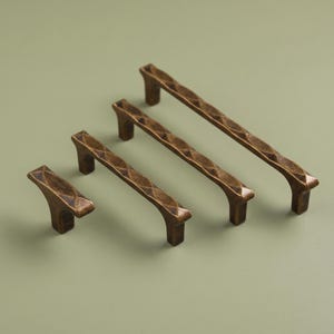 May include: A set of four bronze-toned metal cabinet pulls and a matching knob, each featuring a textured, diamond-patterned surface with a dark, weathered finish. The hardware pieces vary in length, ranging from a single knob to long handles.