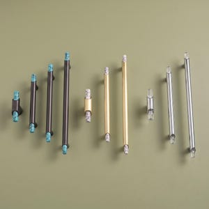 May include: A collection of cabinet hardware including dark brown pulls with turquoise stone accents, gold-toned pulls with white stone accents, and silver-toned pulls with clear acrylic accents, arranged in varying lengths and styles.
