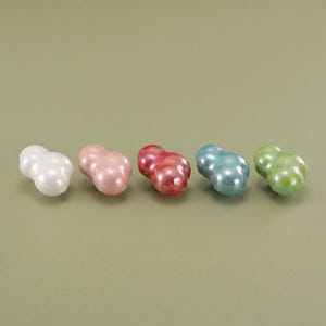May include: Five small, smooth, cloud-shaped objects arranged in a horizontal row. Each piece features a glossy, iridescent finish in distinct colors: white, pale pink, deep red, light blue, and lime green. The shapes are rounded and bulbous.