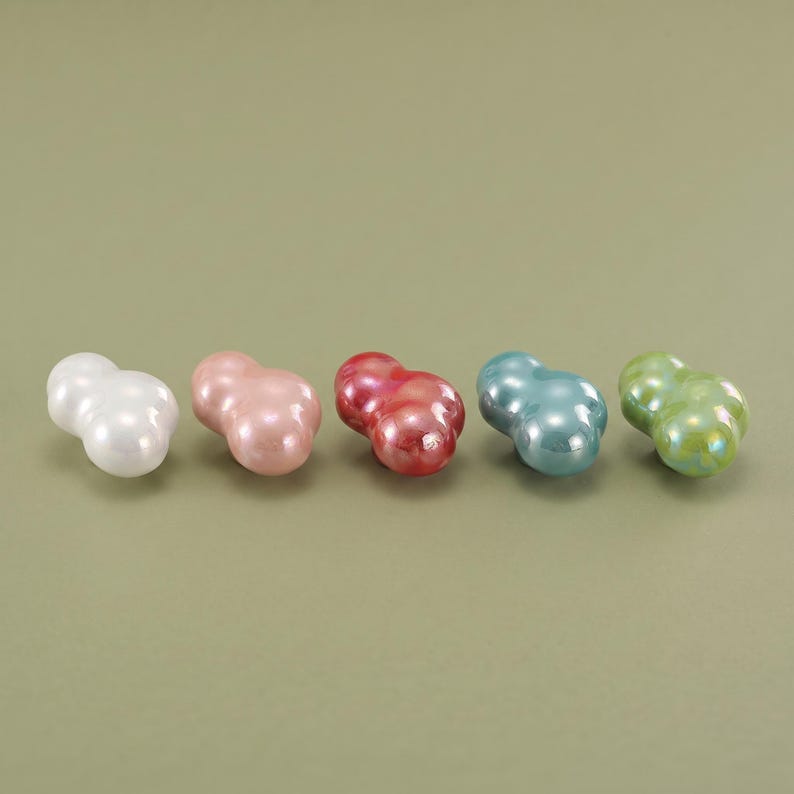 May include: Five small, smooth, cloud-shaped objects arranged in a horizontal row. Each piece features a glossy, iridescent finish in distinct colors: white, pale pink, deep red, light blue, and lime green. The shapes are rounded and bulbous.