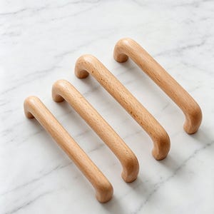 May include: Four light-coloured wooden cabinet handles arranged in a diagonal row. Each handle features a smooth, cylindrical, arched design with rounded ends, showcasing a natural wood grain texture and a consistent, polished finish throughout.