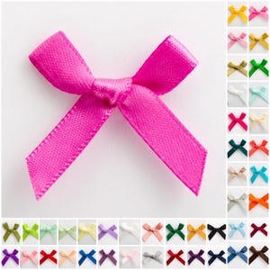 May include: A vibrant fuchsia satin ribbon bow is the focal point, with a selection of smaller bows in various colours arranged below and to the right. These bows are likely for crafts, gift wrapping, or embellishments.