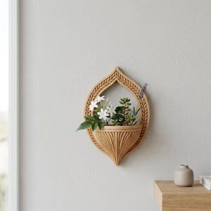 Peut inclure: Un pot mural marron clair avec un design décoratif en forme de feuille. Le pot contient une variété de petites plantes et de fleurs blanches. Le pot est accroché à un mur gris clair.